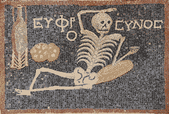 Mosaic of a skeleton resting among loafs of bread, holding a goblet of wine, with text 'Euphrosynos': 'enjoy, have fun, cheer up'.